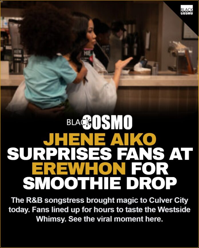 Jhené Aiko Pops Up at Erewhon Culver City to Surprise Fans for New ‘Westside Whimsy’ Smoothie Launch Jhené Aiko smiling and holding a blue Westside Whimsy smoothie behind the counter at Erewhon Culver City.