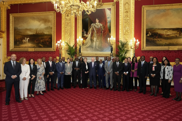King Charles standing with Caribbean officials in a grand room beneath a controversial portrait of King George IV.