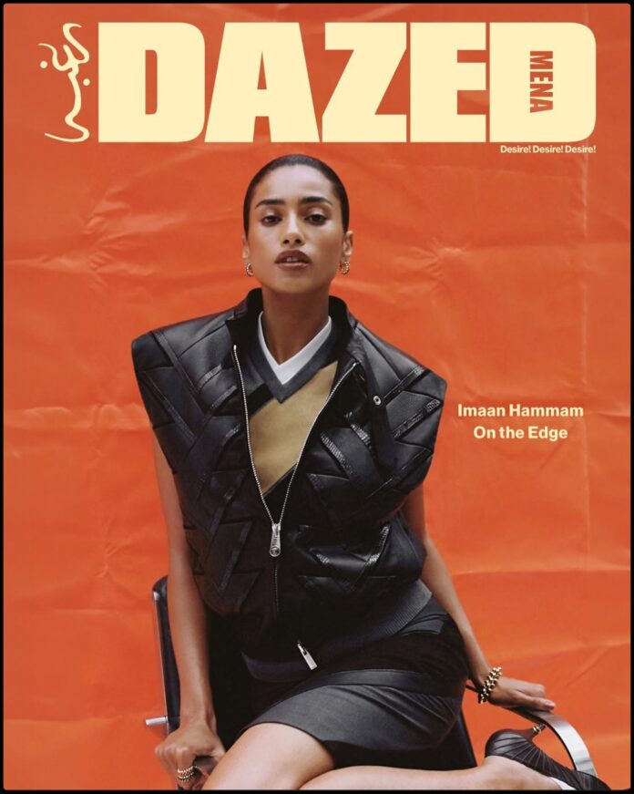 Imaan Hammam on Dazed Middle East April 2026 Imaan Hammam wearing a dark practical jacket, standing with her back to the camera, looking out over a still glacial lake reflecting a snow-capped mountain range at dawn.