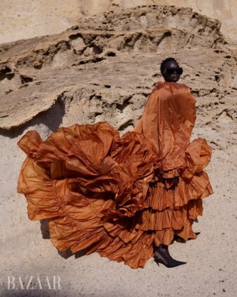 Achol Kuir modeling in the Canary Islands for Harper's Bazaar April 2026, posing against volcanic cliffs in graphic fashion.