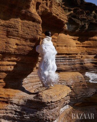 Achol Kuir modeling in the Canary Islands for Harper's Bazaar April 2026, posing against volcanic cliffs in graphic fashion.
