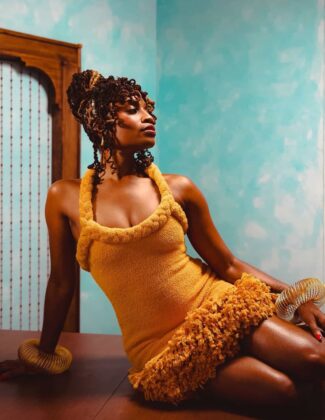 Aleshea Harris on the cover of Hattie Magazine, wearing an ochre garment and gold bangles, flanked by hands offering a crucifix and ancestral cloths.