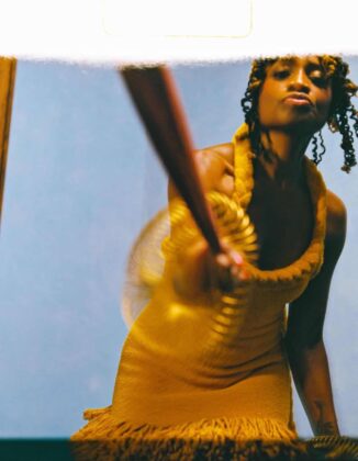 Aleshea Harris on the cover of Hattie Magazine, wearing an ochre garment and gold bangles, flanked by hands offering a crucifix and ancestral cloths.