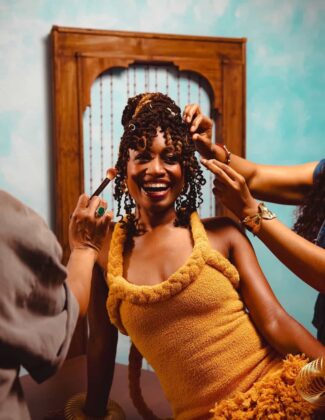 Aleshea Harris on the cover of Hattie Magazine, wearing an ochre garment and gold bangles, flanked by hands offering a crucifix and ancestral cloths.