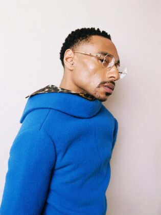 Durand Bernarr posing in a muted lichen green setting with cellular beadwork accessories and textured plumage garments for PAUSE Online June 2026 cover.