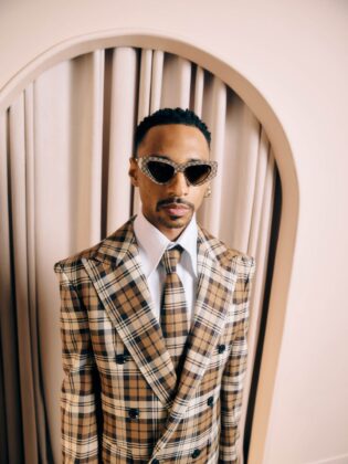 Durand Bernarr posing in a muted lichen green setting with cellular beadwork accessories and textured plumage garments for PAUSE Online June 2026 cover.