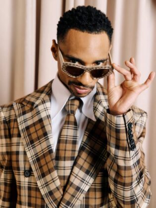 Durand Bernarr posing in a muted lichen green setting with cellular beadwork accessories and textured plumage garments for PAUSE Online June 2026 cover.